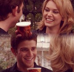 a man holding a beer in front of a woman's face and smiling at him