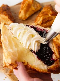 someone is spreading cream on top of a croissant with blueberry toppings