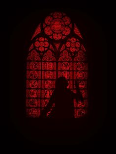 the silhouette of a person standing in front of a stained glass window with red lights