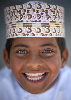 a young boy wearing a white and brown patterned headband smiles at the camera with his eyes wide open