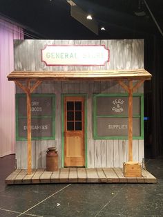 a small wooden building sitting on top of a stage with signs above it that read general store