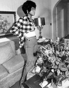 a black and white photo of a woman standing next to a table with flowers on it