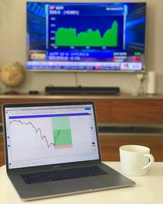 an open laptop computer sitting on top of a table next to a coffee cup and television