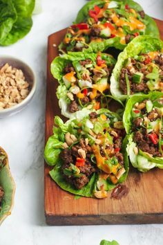 lettuce wraps filled with meat and vegetables on a cutting board next to bowls of rice