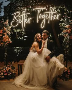 a bride and groom sitting under a neon sign that says better together in front of them