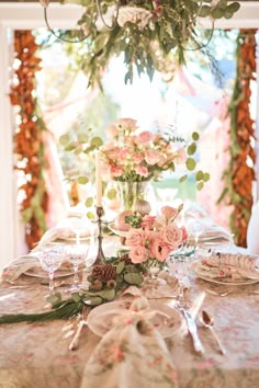 the table is set with pink flowers and greenery on it, along with candlesticks