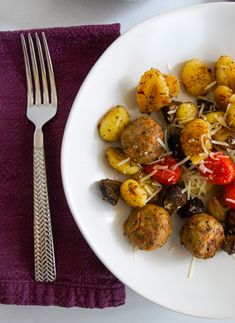 a white plate topped with meatballs covered in cheese and tomatoes next to a fork