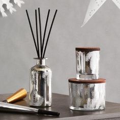 two glass jars with reeds and a pen are on a table next to an ornament