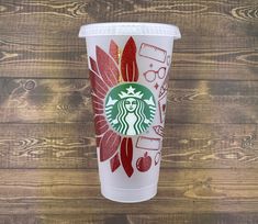 a starbucks cup with red and gold designs on the side sitting on a wooden table