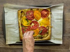 a person placing tomatoes on top of a pizza in a box with paper wrapping around it