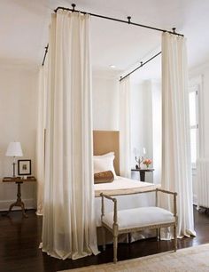 a bedroom with white drapes hanging from the ceiling and a bed in front of it