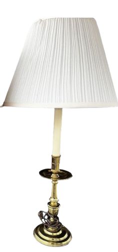 a lamp with a white shade on top of it and a gold plated base