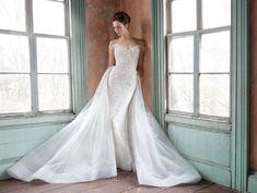 a woman in a white wedding dress standing by an open window