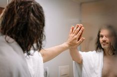 a man with long hair is holding his hands up in front of a bathroom mirror