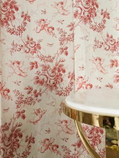 a red and white floral wallpaper in a bathroom with a gold toilet roll holder