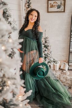 a woman in a green dress standing next to a christmas tree holding a green hat