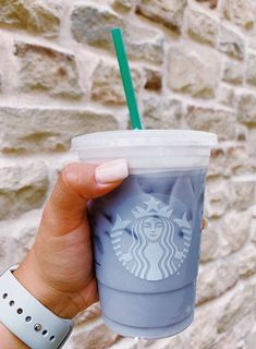 a hand holding a starbucks cup in front of a brick wall with a green straw