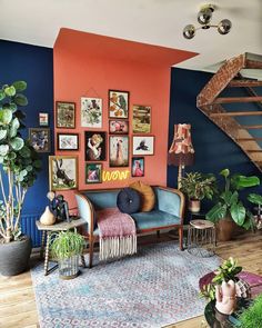 a living room filled with lots of plants and pictures hanging on the wall next to a stair case