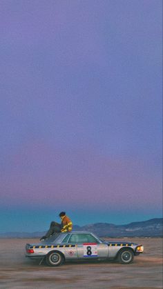 two people sitting on top of a car in the desert