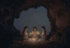 three women sitting in a cave holding candles