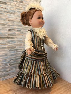 a doll dressed in a striped dress and bonnet is standing on a wooden floor next to a wall