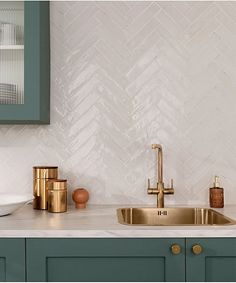 a kitchen sink with gold faucet and green cabinets in front of a white tile backsplash