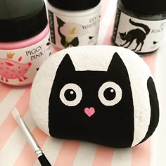 a black and white cat rock sitting on top of a table next to paint bottles