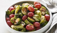 a white bowl filled with brussel sprouts and tomatoes on top of a table