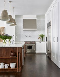 a kitchen with white cabinets and wood flooring is pictured in this image, there are three hanging lights above the island