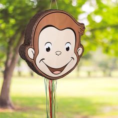 a paper monkey hanging from a string in front of a tree with grass and trees behind it