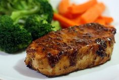 a white plate topped with meat and broccoli next to carrots on a table