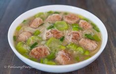 a white bowl filled with meatballs and green peppers on top of a wooden table