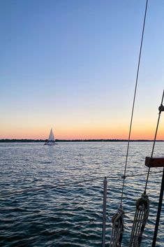 a sailboat sailing on the water at sunset with another boat in the distance behind it