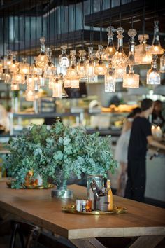 a wooden table topped with lots of bottles and lights hanging from it's ceiling