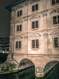 an old building is lit up at night with lights on the windows and water below