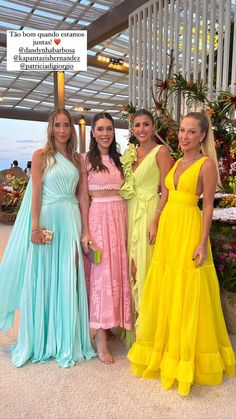 four women in long dresses posing for a photo at an event with one woman wearing a yellow dress