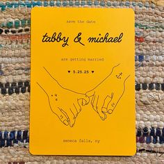 a yellow wedding card with two hands holding each other's hand on top of a rug