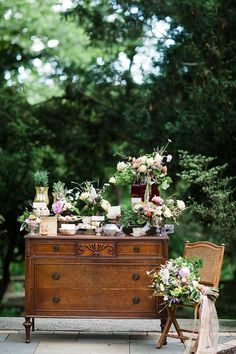 an old dresser with flowers on it and two chairs sitting next to it in front of some trees