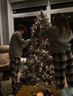 two women decorating a christmas tree in the living room with candles and other decorations