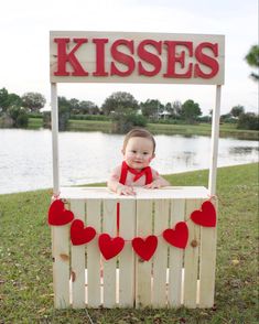 a baby sitting on top of a wooden crate with hearts attached to the box and kissing kisses sign above it