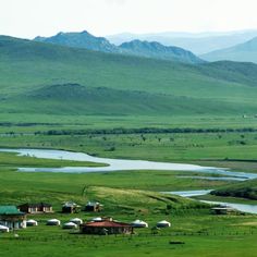 a green field with some buildings and mountains in the background