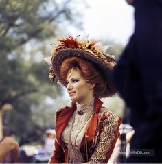 a woman wearing a large hat with feathers on it's head and sitting down