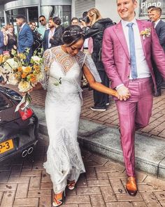 a bride and groom walking down the street holding hands in front of their wedding car