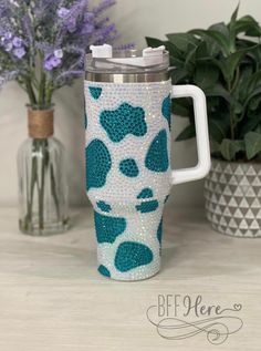 a coffee cup with blue and white designs on it sitting next to some purple flowers