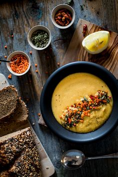 a bowl filled with soup next to sliced bread and other foods on a wooden table