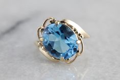 This vintage gold mounting is simple with decorative, sweeping shoulders on the sides and secure prongs. This piece is set with a modern, blue topaz. The color of this stone is deeper, a rich, almost turquoise water color. This would make a lovely cocktail ring, and is also a sturdy enough stone to wear everyday! Metal: 10K Yellow Gold Gem: Blue Topaz 4.46 Carats Gem Measurements: 11.9 x 9.8 mm, Oval Ring Size: 4.25 Classic Blue Topaz Solitaire Ring, Blue Topaz Solitaire Ring For Formal Occasions, Formal Blue Topaz Solitaire Ring, Elegant Blue Topaz Ring In 14k Gold, Formal Blue Solitaire Topaz Ring, Vintage Blue Topaz Ring In 14k Gold, Elegant Turquoise Topaz Gemstone Ring, Blue Oval Topaz Ring In Art Deco Style, Elegant Turquoise Blue Topaz Ring