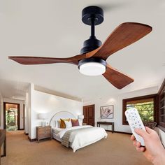 a person is holding a remote control in front of a bed with a ceiling fan