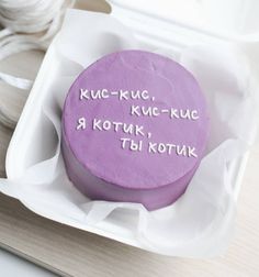 a purple cake with writing on it sitting in a white box next to some spools of thread