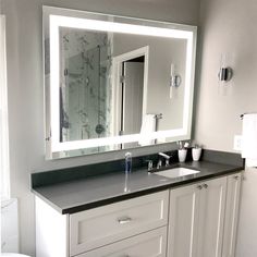 a bathroom with a large mirror above the sink and a white toilet in front of it