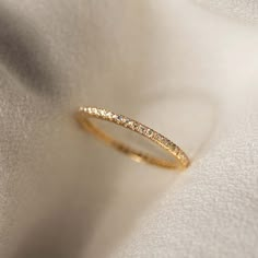 a gold wedding band with small diamonds on it's side, sitting on a white cloth